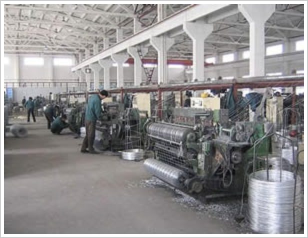 Operators working at wire mesh looms in an open-span hall, wire coils at the machine base