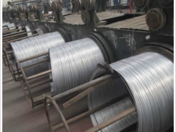 Coils of galvanized wire loaded on feed racks beside the machines